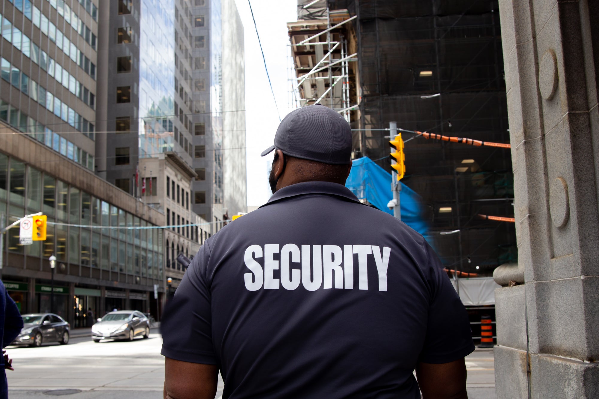 Security guard walking down the street of a city wearing a navy shirt that says Security in big block letters on the back